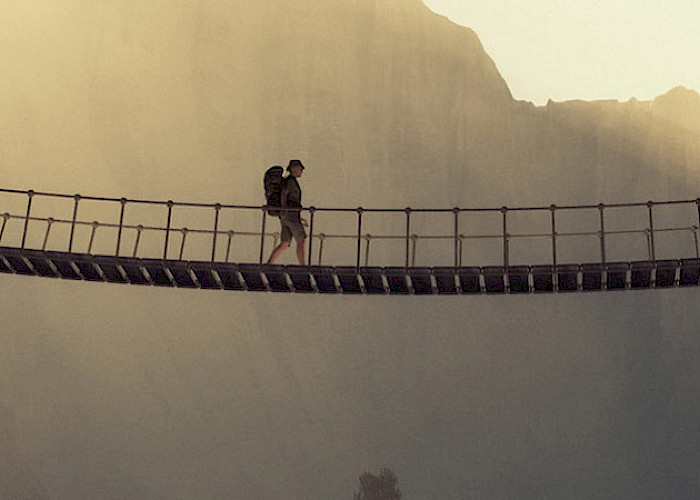 Symbolbild für das Thema Selbsterfahrung / Persönlichkeitsentwicklung Mann mit Rucksack geht über eine Hängebrücke - ©